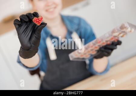 Confectioner holds sweet Belgian chocolate candies on kitchen background. Small business home concept Stock Photo