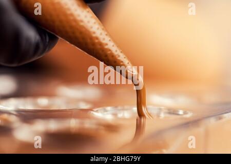 Chef or chocolatier pouring melted dark chocolate into silicone molds on pastry bag Stock Photo