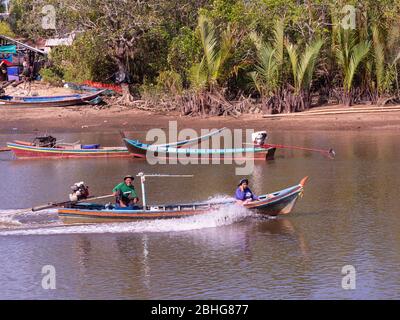 Small long tail boat with man and woman on board on Mak Bang, Satun City, Satun in the south of Thailand. Boat building workshop in the background. Stock Photo