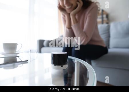 Happy woman looking at compact voice assistant on glass table. Stock Photo