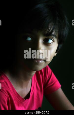 Portrait of an Indian little girl with short hair. Beautiful eye of a child on black background. Dramatic look of a little girl in India. Stock Photo