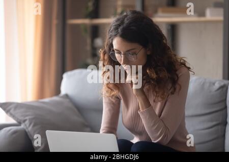 Thoughtful young pretty female freelancer working remotely on laptop. Stock Photo