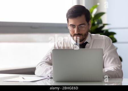 Young serious businessman working at laptop in office. Stock Photo