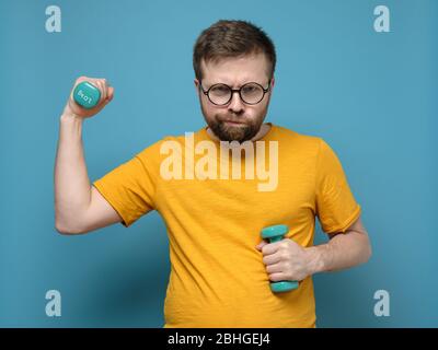 Strange man with round glasses overweight decided to go in for sports, took small dumbbells in hands and was ready for training. Stock Photo