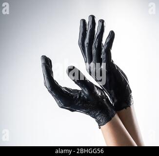 Elegant female hand in black latex glove on a white background. Female hand in liquid black oil or black acrylic paint Stock Photo