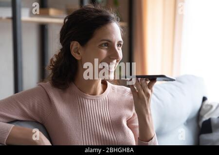 Attractive smiling millennial woman recording voice message on smartphone. Stock Photo