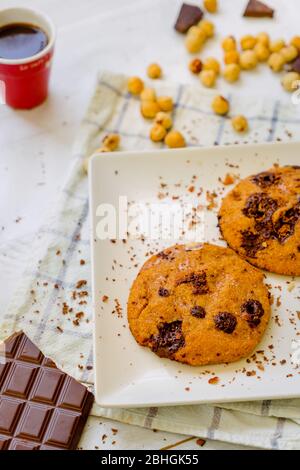 Organic chocolate chip cookies with hazelnuts and coffee in a square plate on a wooden table Stock Photo