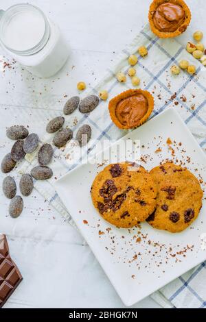 Organic chocolate chip cookies with hazelnuts, coconut milk and chocolate candies in a square plate on a wooden table Stock Photo