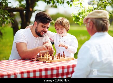 happy family of three generation of men playing chess in spring garden Stock Photo