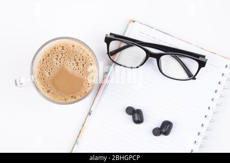 Cup of coffee, note book, Wireless Bluetooth headphones and eye glasses are isolated on white background Stock Photo