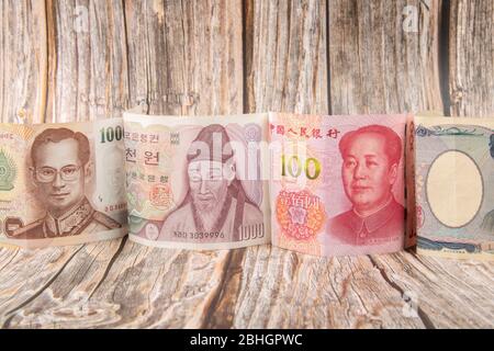 Close up portrait banknotes of Thai Baht, Korea Won and China RMB Yuan on wooden background. Finance and business concept Stock Photo