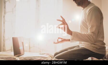 power of meditation, man sitting on the bed in yoga rock position, practicing online at home, details of the hands in surya Mudra e gyan Mudra with fi Stock Photo