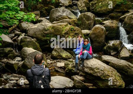 Female tourists posing for photo on boulders at Torc Waterfall in Killarney National Park, County Kerry, Ireland Stock Photo
