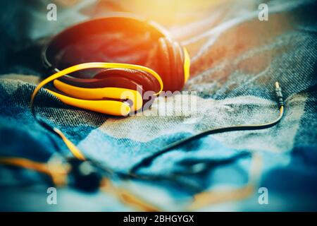 Bright yellow headphones with a microphone for listening to music lie on a soft blue plaid wool blanket and are illuminated by sunlight. Time for insp Stock Photo