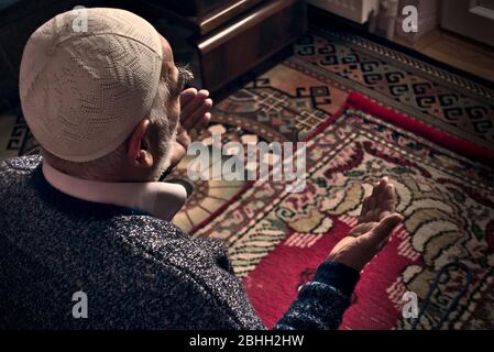 Very old bearded Turkish Muslim man at his 80's with a prayer cap praying to Allah at his home on his prayer in Ramadan month Stock Photo