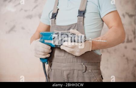 Portrait man builder repairer in protective glasses, hard hat, overalls showing having equipment in arm on grey background home brick Stock Photo