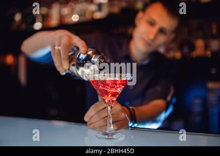 Barman is preparing mix cocktail in shaker of red alcohol and ice glass, bar counter Stock Photo