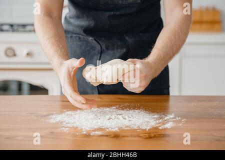 Hands of experienced chef man in apron preparing pizza dough on wooden table. Light background close-up Stock Photo