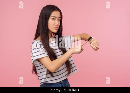 Hurry up, it's late. Portrait of displeased angry girl with long brunette hair pointing at wrist watch, checking time on clock and worrying about dela Stock Photo