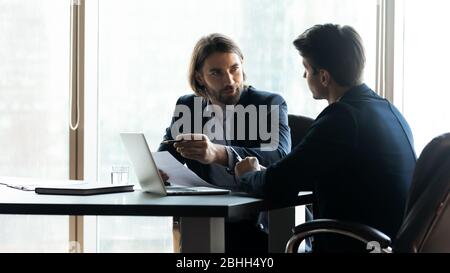 Confident businessman pointing at laptop screen, discussing strategy Stock Photo