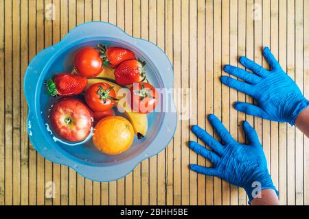 Cleaning the fruit with water and lye to eliminate the spread of the coronavirus. Hands with blue latex gloves and a blue bowl with different fresh an Stock Photo
