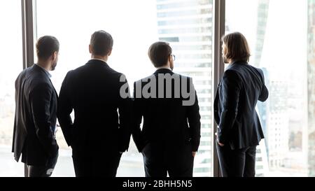 Rear view four confident successful businessmen looking through window Stock Photo