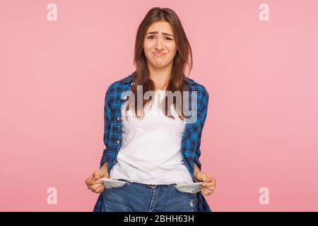 Poor student, unemployment. Portrait of upset jobless girl in checkered shirt turning out empty pockets, showing no money gesture, worried about debts Stock Photo