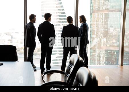 Rear view four confident businessmen looking through panoramic window Stock Photo