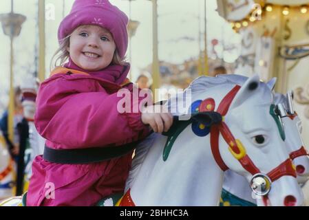 A young girl on a merry-go-round, carousel at a fairground, funfair, amusement park, England, UK Stock Photo