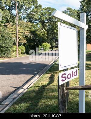 A house for sale sign hanging from a post with a sold sign under it for a corner house. Stock Photo