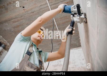 Builder worker cutting electrical chase in concrete wall with circulation saw drill diamond crown Stock Photo