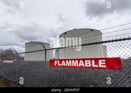 Large jet fuel or oil storage tanks behind a chain link fence with warning signs. Stock Photo