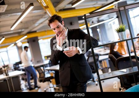 Handsome young businessman wearing black suit using modern smartphone in the office Stock Photo