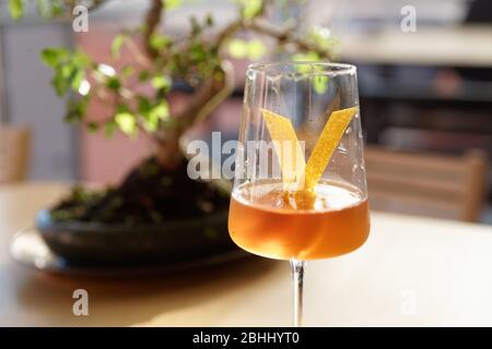 Japanese style cocktail with lemon zest in wineglass, bonsai tree in the background Stock Photo