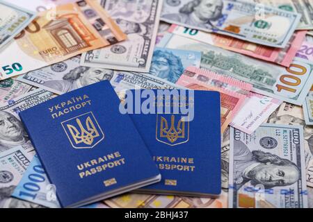 Two Ukrainian biometric passports lie against a background of currencies from different countries of the world, euros, dollars, hryvnias, forints. The Stock Photo