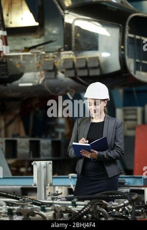 Portrait of a female factory manager in a white hard hat and business suit. Controlling the work process at the airplane manufacturer. Stock Photo