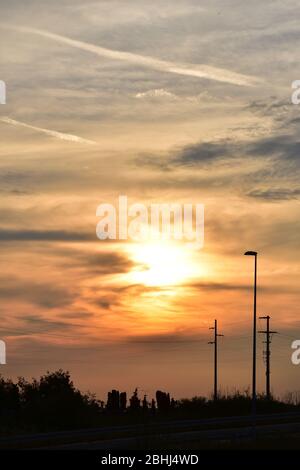 A thin layer of clouds obscures the sun at sunset. Orange gray in the sky and silhouettes on the earth Stock Photo