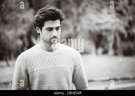 Handsome man outdoors in a park. Portrait of a beautiful young man outdoors. Cut trendy hair, slight beard. Winter clothes. Black and white. Stock Photo