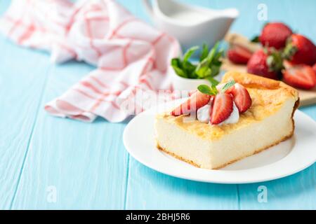 Cottage cheese casserole or pudding with fresh summer strawberries on blue wooden table, copy space for text or design elements. Breakfast cheese cake Stock Photo