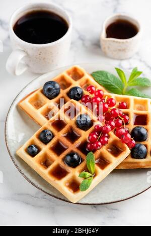 Belgian waffles with fresh summer berries, maple syrup and cup of black coffee Stock Photo