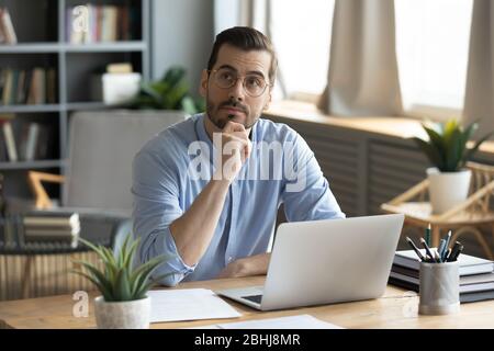 Thoughtful businessman wearing glasses touching chin, pondering ideas Stock Photo