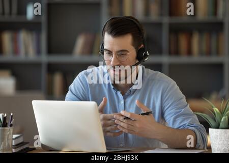 Confident man teacher wearing headset speaking, holding online lesson Stock Photo