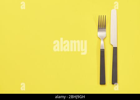Black knife and fork on yellow background. Top view Stock Photo