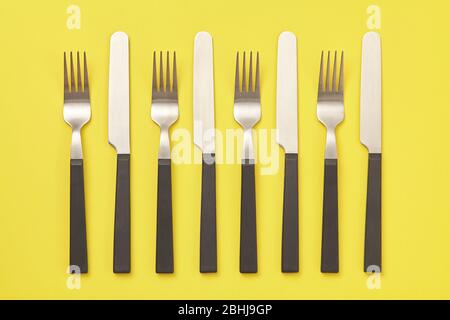 Black knife and fork on yellow background. Top view Stock Photo