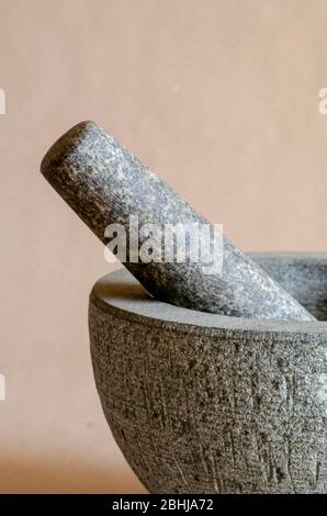 Fragment of a gray mortar with a pestle. Close-up of kitchen utensils on a beige background. The texture of the stone. Selective focus. Stock Photo