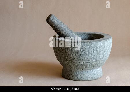 Gray stone mortar with pestle. Close-up of a kitchen granite mortar on a beige background. Copy space. Selective focus. Stock Photo