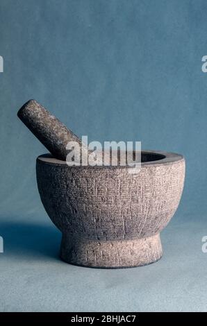 Gray stone mortar with pestle. Close-up of a kitchen granite mortar on a blue background. Copy space. Selective focus. Stock Photo