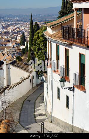 Empty charming narrow street between residential houses leading up to Sierra Nevada mountains, down to old town of Granada resort town. Sunny day Stock Photo