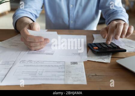 Close up man checking bills, holding receipt, using calculator Stock Photo