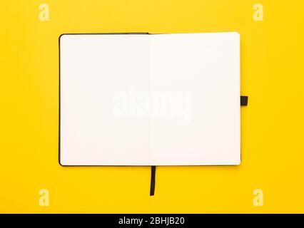 Black notebook opened isolated on yellow background. Stock Photo